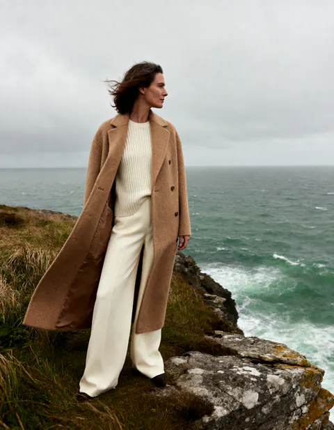 Femme en manteau camel au bord d'une falaise